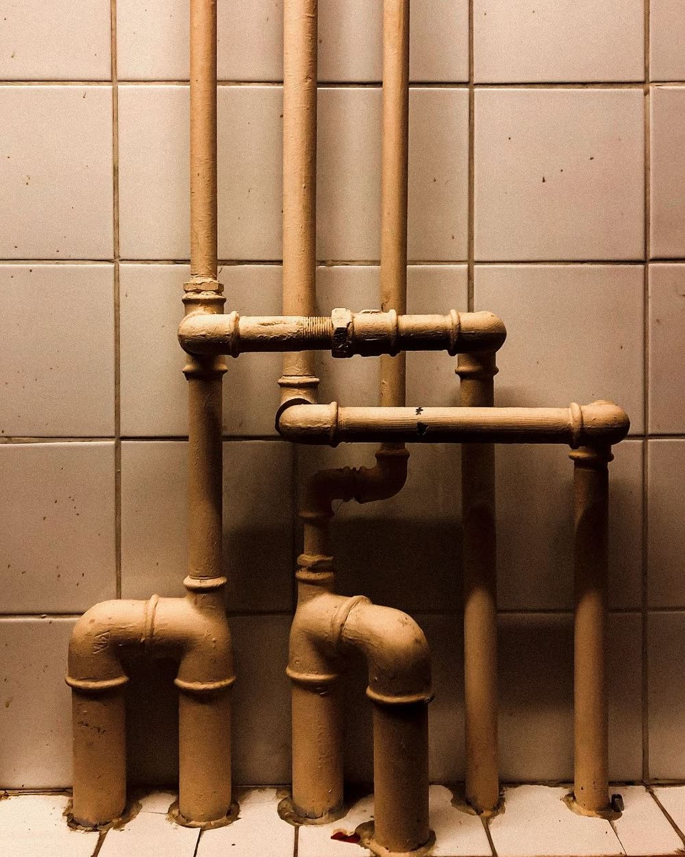 Tubería antigua de baño con conexiones y codos junto a azulejo